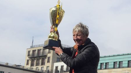 Dieses Foto zeigt die Rallye Legende Heide Hetzer mit einem Pokal am Brandenburger Tor.
