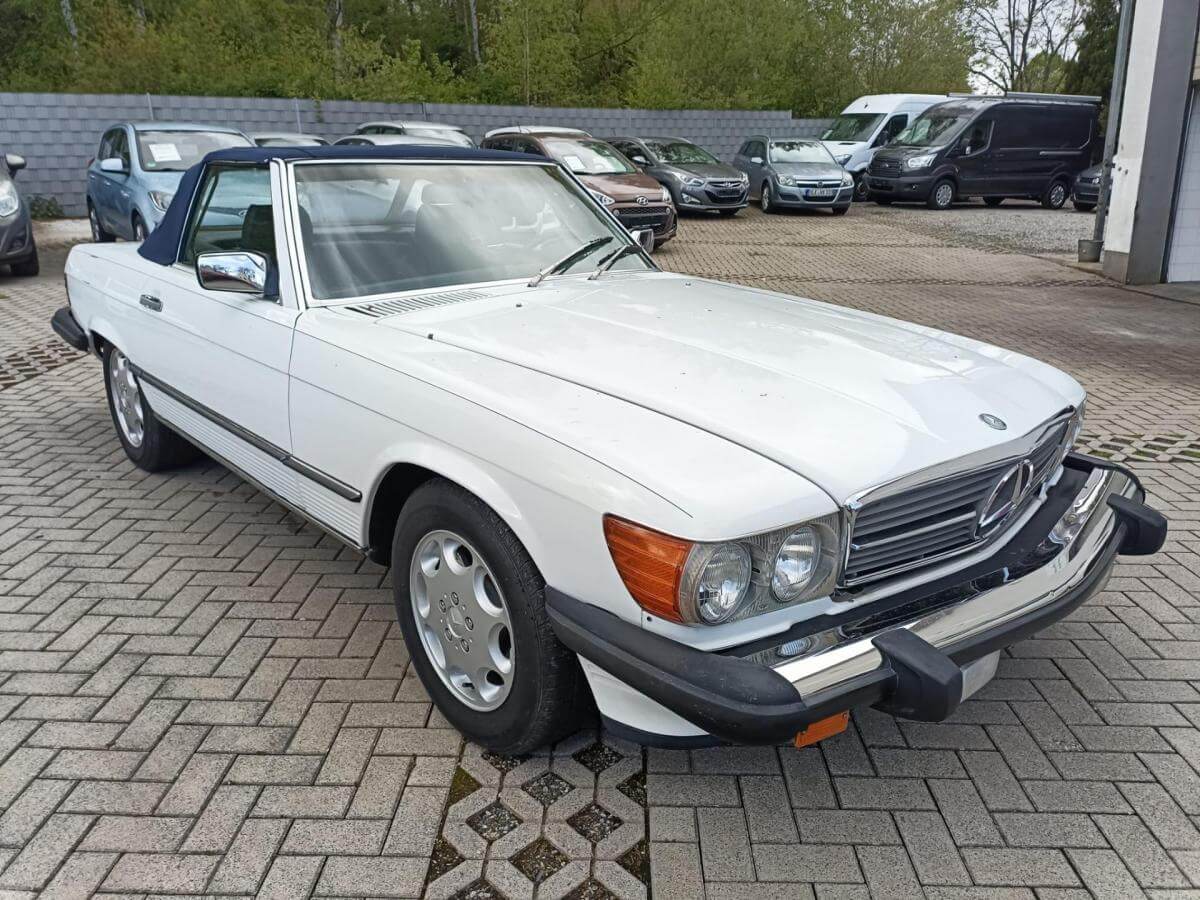 Dieses Foto zeigt den Mercedes-Benz 560 SL R 107, einen Oldtimer von 1987 in Artikweiß/Royal Blau. Das Fahrzeug ist technisch und optisch top gepflegt. V8-Power, Automatik und H-Kennzeichen sorgen für entspanntes Cruisen mit klassischem Charme. Ein eleganter Roadster für Liebhaber – bereit für die nächste Ausfahrt. Biete jetzt mit und ersteigere diesen Klassiker.